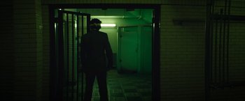 Movie still from “Sorry to Bother You” (2018), directed by Boots Riley – A man standing in a dark room next to a door way; Wide shot, Low angle