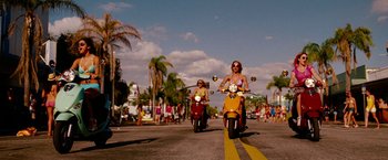 Movie still from “Spring Breakers” (2012), directed by Harmony Korine – Two people riding scooters down a street with palm trees in the background; Wide shot, Low angle