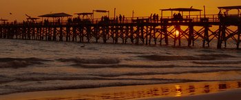 Movie still from “Spring Breakers” (2012), directed by Harmony Korine – A group of people standing on a pier near the ocean; Extreme Wide shot, High angle