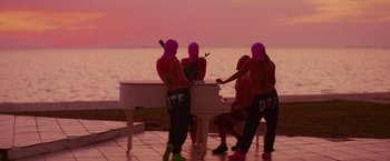 Movie still from “Spring Breakers” (2012), directed by Harmony Korine – A group of people dressed in pink and purple costumes playing a piano; Extreme Wide shot, Over the shoulder angle