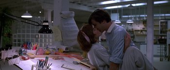 Movie still from “St. Elmo's Fire” (1985), directed by Joel Schumacher – A man and a woman kissing in front of a desk; Medium shot, Low angle