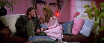 Two people are sitting on a couch and one is holding a drink