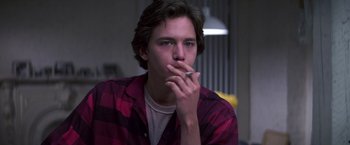 Movie still from “St. Elmo's Fire” (1985), directed by Joel Schumacher – A young man smoking a cigarette in a room; Medium shot, Low angle