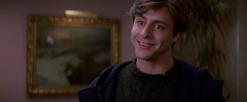 Movie still from “St. Elmo's Fire” (1985), directed by Joel Schumacher – A young man smiling for the camera in front of a painting; Close Up shot, Over the shoulder angle