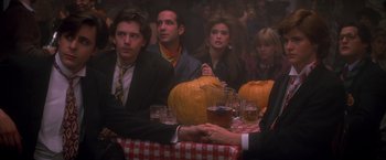 Movie still from “St. Elmo's Fire” (1985), directed by Joel Schumacher – A group of people sitting at a table with pumpkins on it; Medium shot, Over the shoulder angle