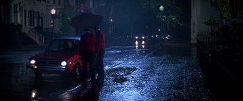 Movie still from “St. Elmo's Fire” (1985), directed by Joel Schumacher – Two people standing in the middle of the street under an umbrella; Wide shot, High angle