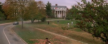 Movie still from “St. Elmo's Fire” (1985), directed by Joel Schumacher – A group of people standing on top of a lush green field; Extreme Wide shot, High angle
