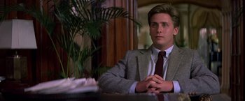 Movie still from “St. Elmo's Fire” (1985), directed by Joel Schumacher – A man sitting at a table in front of a potted plant; Medium shot, Low angle