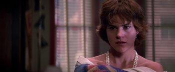 Movie still from “St. Elmo's Fire” (1985), directed by Joel Schumacher – A woman with a pearl necklace and a plaid dress; Close Up shot, Over the shoulder angle