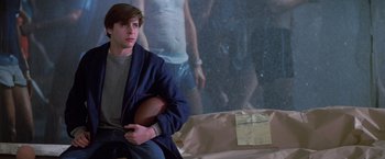 Movie still from “St. Elmo's Fire” (1985), directed by Joel Schumacher – A young man holding a football in front of a picture; Medium shot, Over the shoulder angle