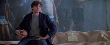 Movie still from “St. Elmo's Fire” (1985), directed by Joel Schumacher – A man sitting on a couch in front of a wall; Medium shot, Low angle