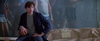 Movie still from “St. Elmo's Fire” (1985), directed by Joel Schumacher – A man sitting on top of a couch in front of a painting; Medium shot, Low angle