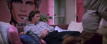 Movie still from “St. Elmo's Fire” (1985), directed by Joel Schumacher – A man sitting on top of a couch in a living room; Medium shot, Low angle