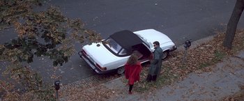 Movie still from “St. Elmo's Fire” (1985), directed by Joel Schumacher – Two people standing in front of a car with an open trunk; Wide shot, High angle