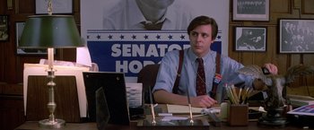 Movie still from “St. Elmo's Fire” (1985), directed by Joel Schumacher – A man sitting at a desk in front of an election poster; Medium shot, High angle