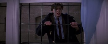 Movie still from “St. Elmo's Fire” (1985), directed by Joel Schumacher – A man in a suit and tie behind bars; Medium shot, Low angle