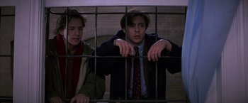 Movie still from “St. Elmo's Fire” (1985), directed by Joel Schumacher – Two young men standing next to each other behind bars; Medium shot, Low angle