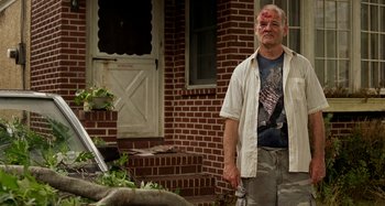Movie still from “St. Vincent” (2014), directed by Theodore Melfi – A man with a bruised face standing in front of a brick house; Medium shot, Low angle