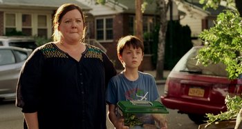 A woman and a boy are standing in front of a car