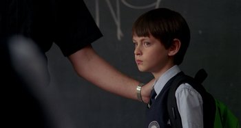 Movie still from “St. Vincent” (2014), directed by Theodore Melfi – A young boy standing in front of a chalkboard with his arm raised; Close Up shot, Over the shoulder angle