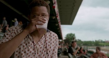 Movie still from “St. Vincent” (2014), directed by Theodore Melfi – A man drinking from a cup in front of a crowd of onlookers; Close Up shot, Over the shoulder angle