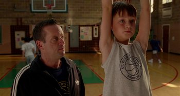 Movie still from “St. Vincent” (2014), directed by Theodore Melfi – A man standing next to a young boy in a gymnasium; Medium shot, Over the shoulder angle