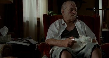 Movie still from “St. Vincent” (2014), directed by Theodore Melfi – An older man smoking a cigarette while sitting in a chair; Medium shot, Low angle