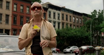 Movie still from “St. Vincent” (2014), directed by Theodore Melfi – An older man standing on the side of the road holding a banana; Medium shot, Low angle