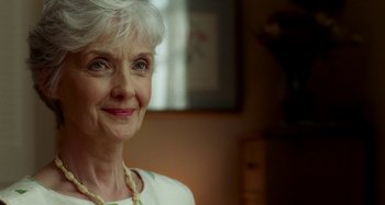 Movie still from “St. Vincent” (2014), directed by Theodore Melfi – An older woman with white hair smiling for the camera; Close Up shot, Over the shoulder angle
