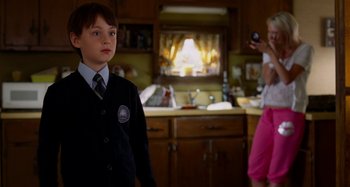 Movie still from “St. Vincent” (2014), directed by Theodore Melfi – A young boy in a suit stands in a kitchen; Medium shot, Over the shoulder angle