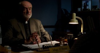 Movie still from “St. Vincent” (2014), directed by Theodore Melfi – A man sitting at a desk in front of a lamp; Medium shot, Over the shoulder angle