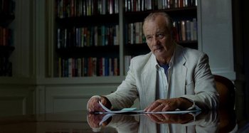 Movie still from “St. Vincent” (2014), directed by Theodore Melfi – An older man sitting at a table in front of a bookshelf; Medium shot, Over the shoulder angle