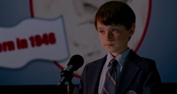 Movie still from “St. Vincent” (2014), directed by Theodore Melfi – A boy in a suit and tie is standing at a microphone; Close Up shot, Over the shoulder angle
