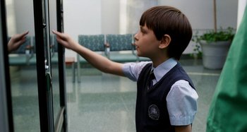 Movie still from “St. Vincent” (2014), directed by Theodore Melfi – A young boy in a school uniform is looking at a wall; Medium shot, Over the shoulder angle