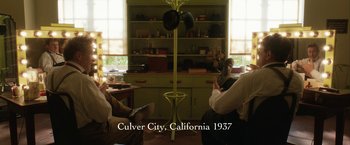 Movie still from “Stan & Ollie” (2018), directed by Jon S. Baird – People sitting in a living room in front of a green cabinet; Wide shot, High angle