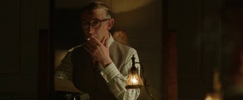 Movie still from “Stan & Ollie” (2018), directed by Jon S. Baird – An older man smoking a cigarette in a dimly - lit room; Medium shot, Over the shoulder angle