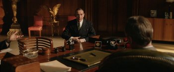 Movie still from “Stan & Ollie” (2018), directed by Jon S. Baird – A man sitting at a desk in front of a phone; Medium shot, Over the shoulder angle