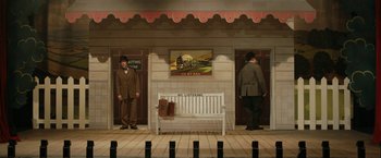 Movie still from “Stan & Ollie” (2018), directed by Jon S. Baird – Two men standing in front of a white bench in front of a train station; Extreme Wide shot, High angle