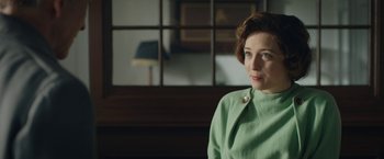 Movie still from “Stan & Ollie” (2018), directed by Jon S. Baird – A woman sitting in a chair wearing a green jacket; Medium shot, Over the shoulder angle