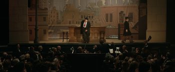 Movie still from “Stan & Ollie” (2018), directed by Jon S. Baird – A man sitting at a table in front of an audience; Wide shot, High angle