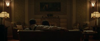 Movie still from “Stan & Ollie” (2018), directed by Jon S. Baird – A man and a woman sitting on a couch in front of a television; Medium shot, Over the shoulder angle