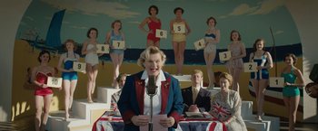 Movie still from “Stan & Ollie” (2018), directed by Jon S. Baird – A woman is speaking into a microphone in front of a group of people; Medium shot, Low angle