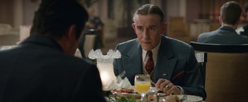 Movie still from “Stan & Ollie” (2018), directed by Jon S. Baird – An older man sitting at a dinner table with a drink; Close Up shot, Over the shoulder angle