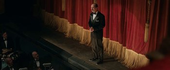 Movie still from “Stan & Ollie” (2018), directed by Jon S. Baird – A man standing on a stage in front of a red curtain; Wide shot, Low angle