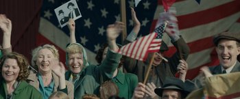 Movie still from “Stan & Ollie” (2018), directed by Jon S. Baird – A group of people in a crowd holding american flags; Medium shot, Over the shoulder angle