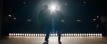 Movie still from “Stan & Ollie” (2018), directed by Jon S. Baird – Two men standing in front of a stage lit by lights; Wide shot, Low angle