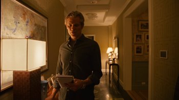 Movie still from “Full Circle” (2023), directed by Steven Soderbergh – A man standing in a hallway holding a notebook; Medium shot, Low angle