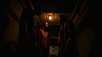 Movie still from “Full Circle” (2023), directed by Steven Soderbergh – A group of people standing around in a dark room; Medium shot, Low angle