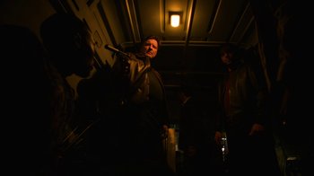 Movie still from “Full Circle” (2023), directed by Steven Soderbergh – A man standing in a dark room holding a cane; Medium shot, Low angle