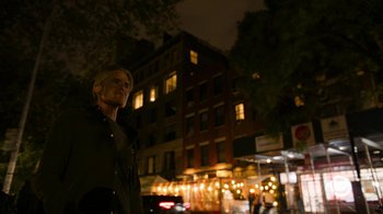 Movie still from “Full Circle” (2023), directed by Steven Soderbergh – A man standing in front of a building at night; Medium shot, Low angle